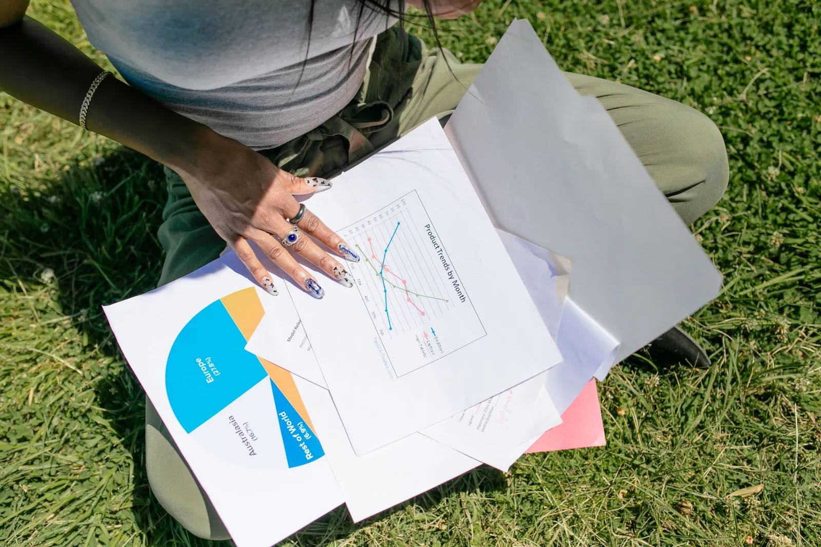 A woman sitting on grass analyzing business documents with charts and graphs in sunlight. How to Read Degree Outcomes Before Choosing a Program
