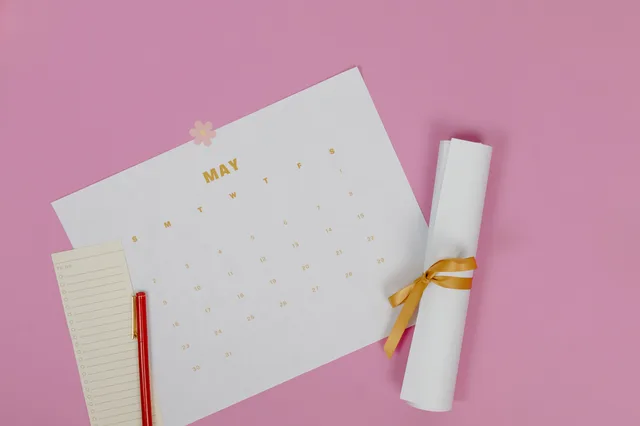 Flat lay of a May calendar with a pen and paper roll on pink background. 7 points worth checking on MBA programs admissions